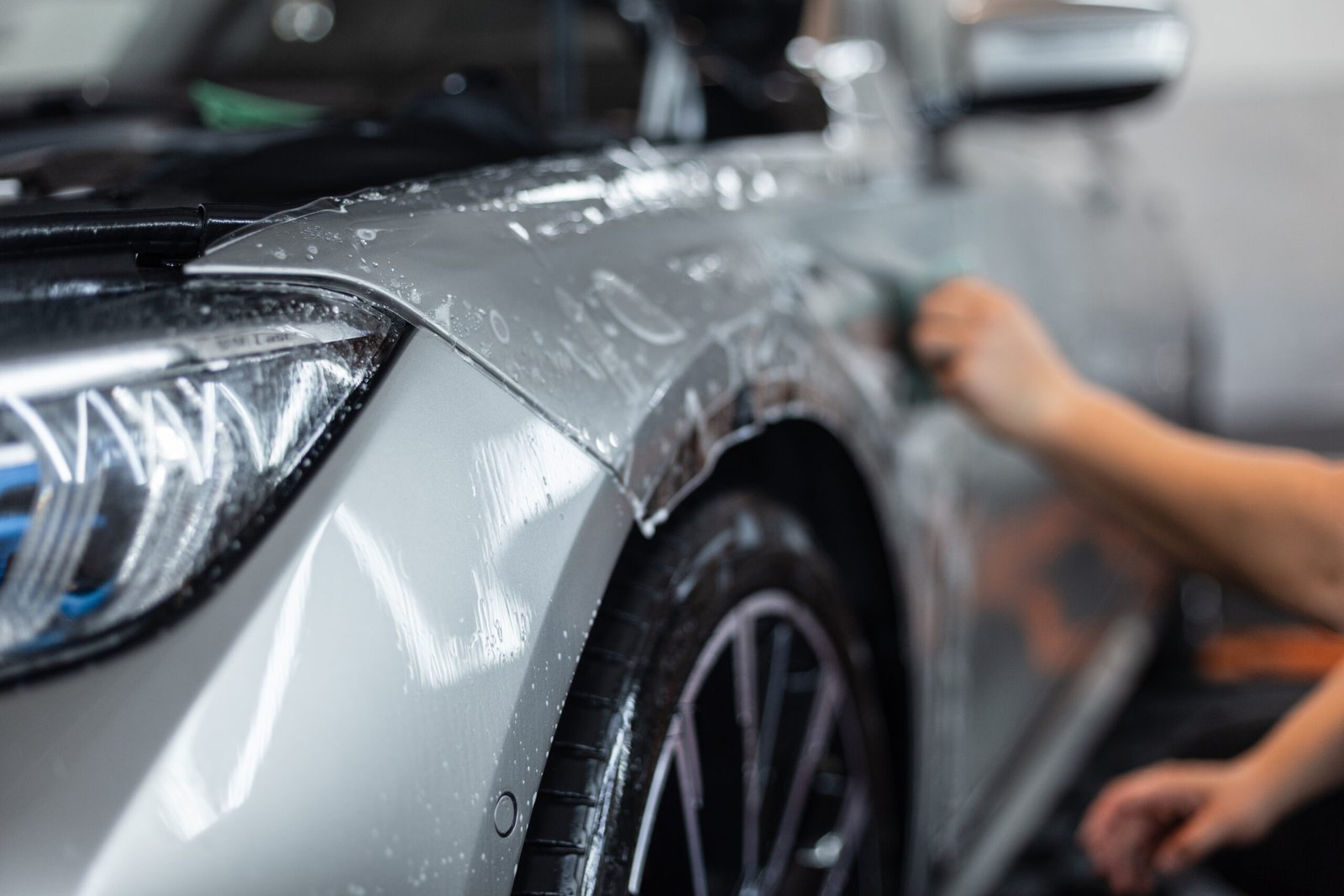 professional man will cover a car with protective PPF film at a detailing service.