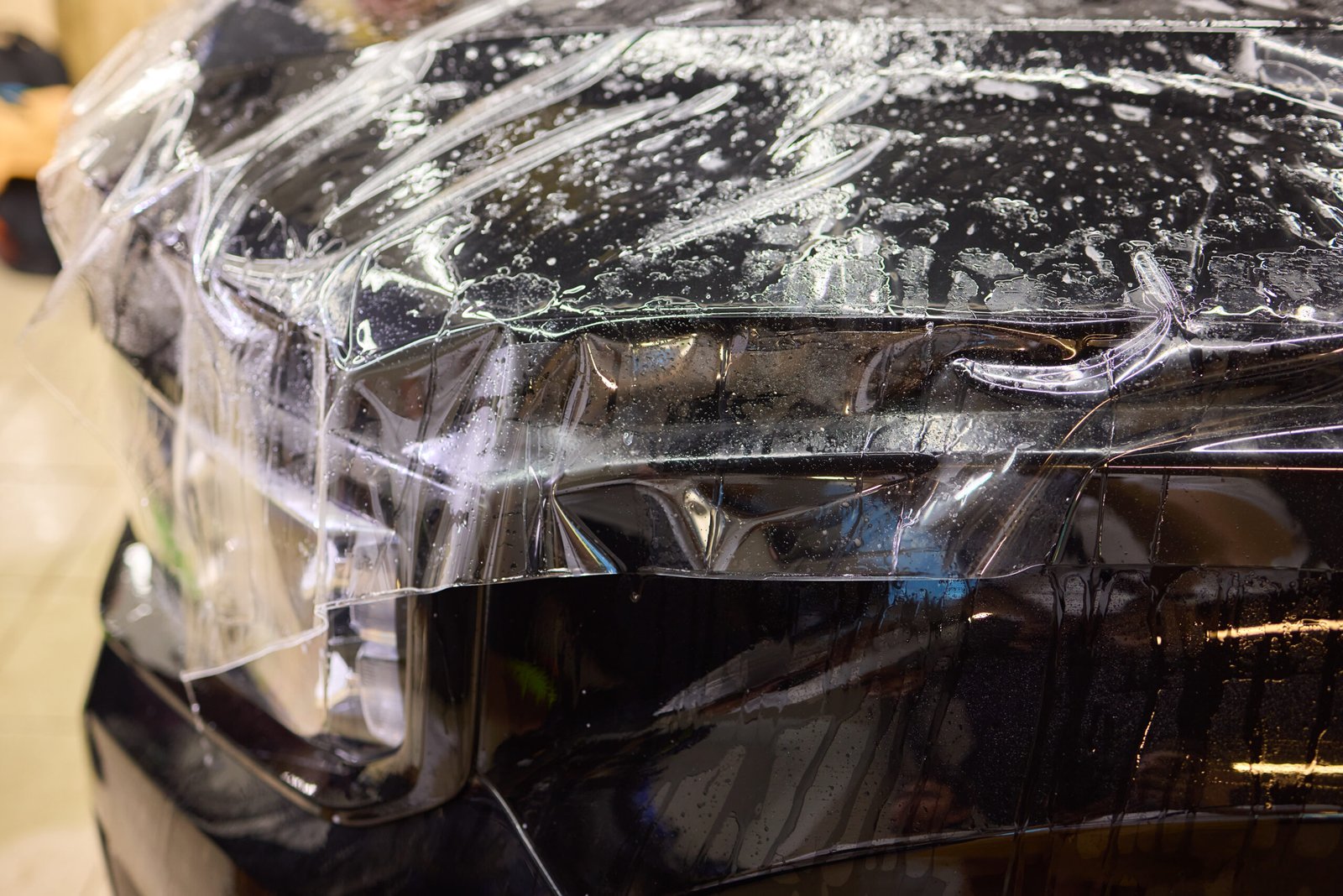 A mechanic is applying a protective film to the car headlight for protection of both paint and headlight itself